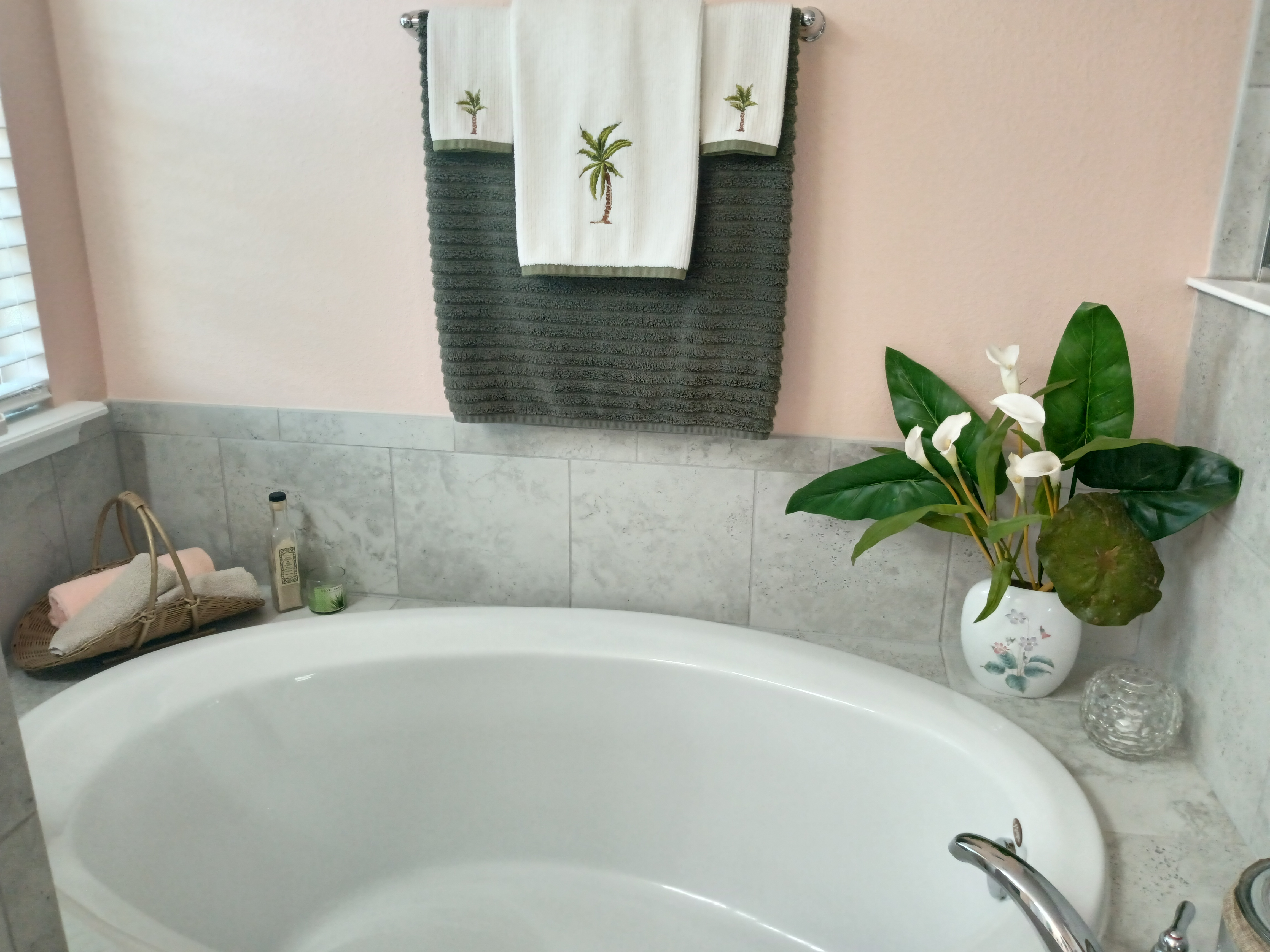 Master bathroom soaking tub with marble tile and palm tree towels
